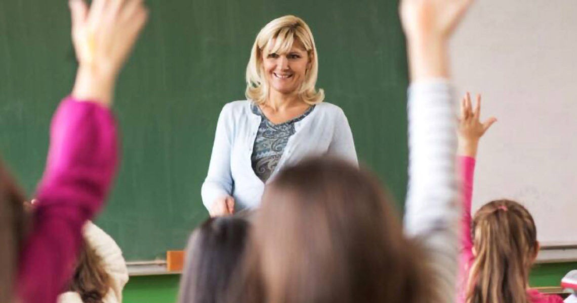 A schoolteacher addressing a class of students with their hands raised